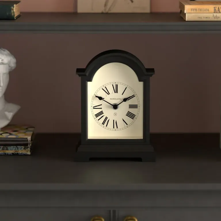 Black mantel clock with Roman numerals on shelf