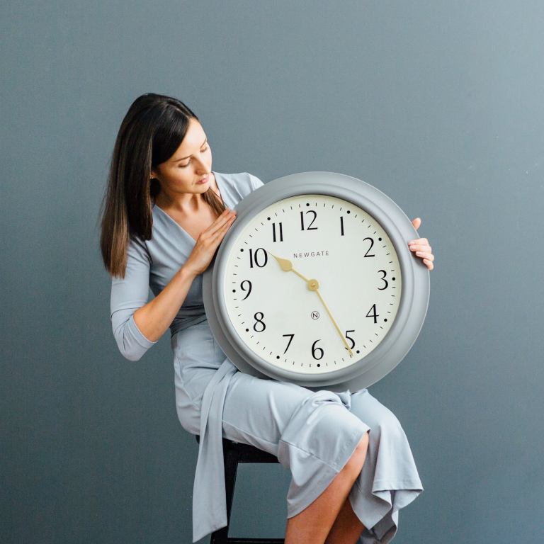 Woman holding large wall clock indoors