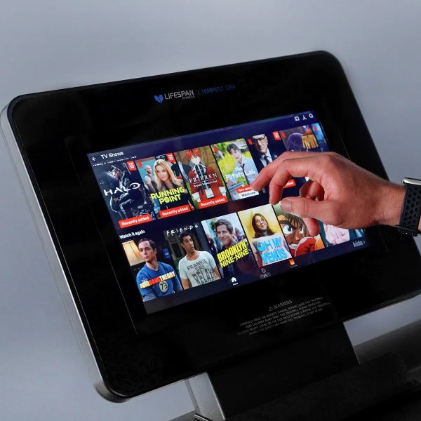 lifespan fitness tempest crx commercial smart treadmill with 15.6 tft touch display" Hand selecting TV show on treadmill touchscreen