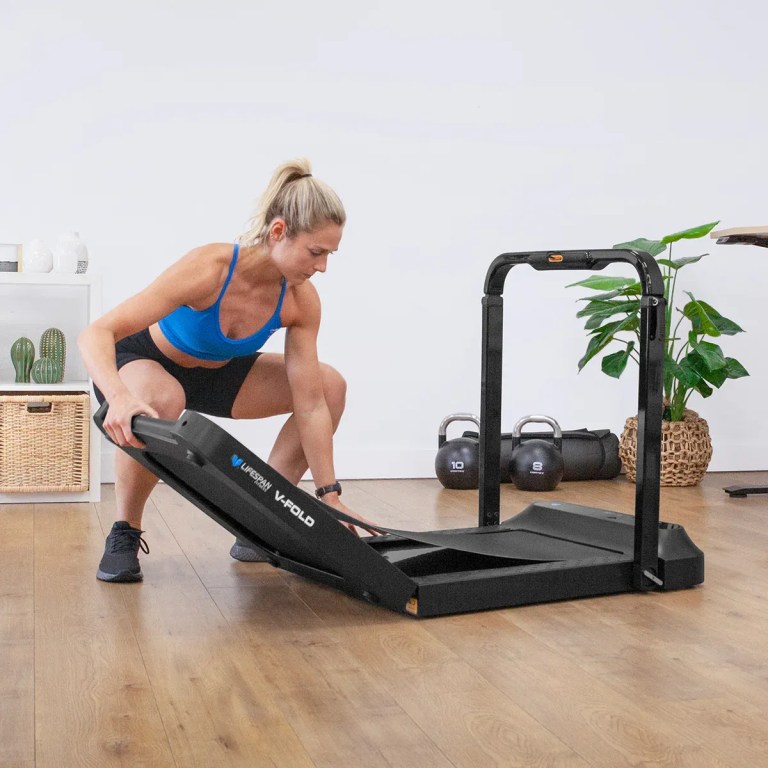 Woman folding compact treadmill in home gym