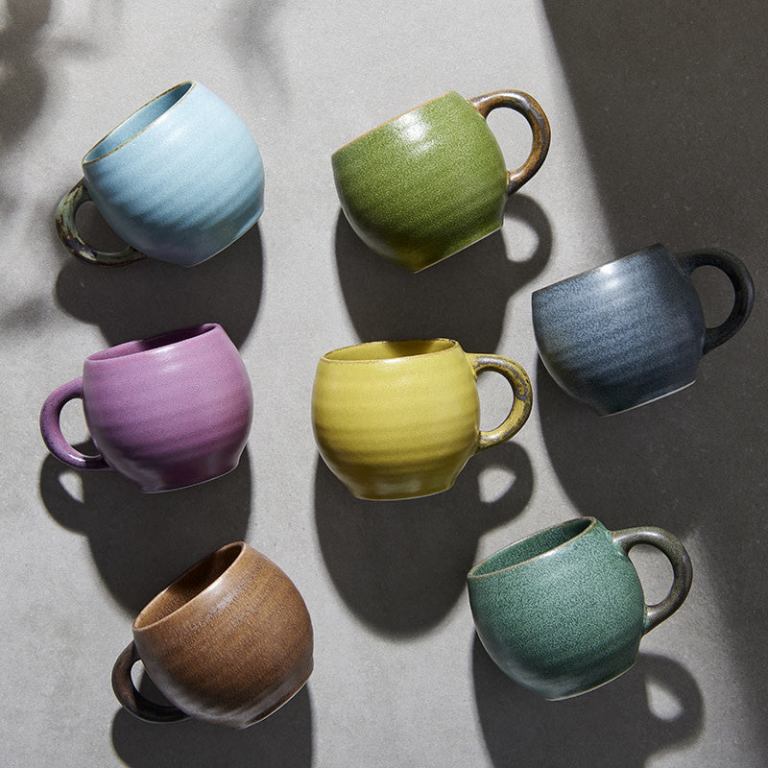 Seven colourful ceramic mugs on light surface