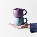 Hand holding two stacked ceramic mugs