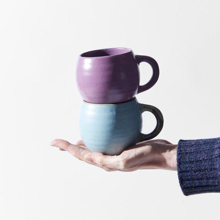 Hand holding two stacked ceramic mugs