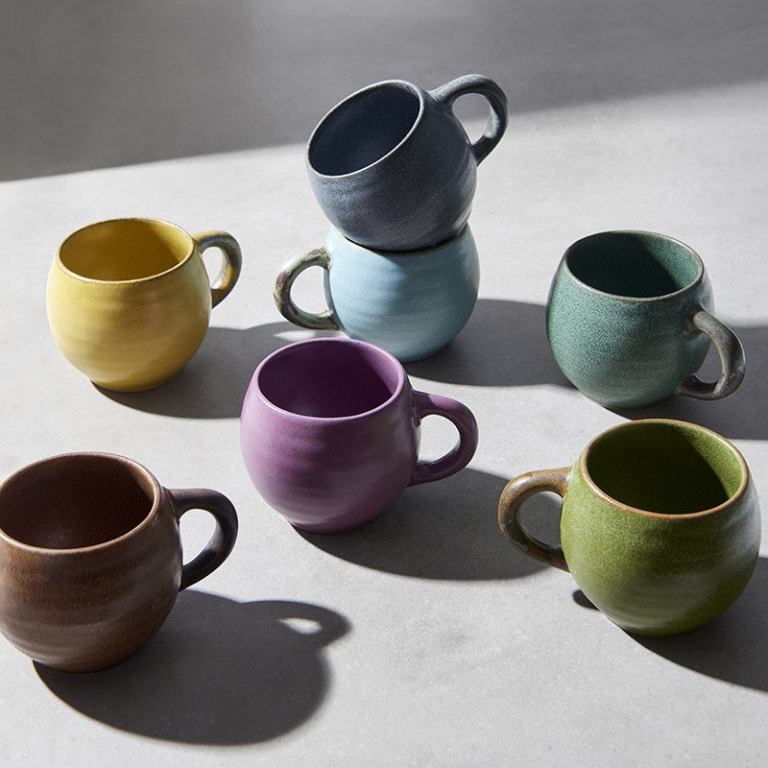 Colourful ceramic mugs arranged on light surface