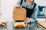 Person holding bamboo lunchbox over glass container
