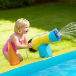 inflatable bounce house, 3.82 x 3.98 x 1.97 m inflatable bounce house water slide, bouncer castle with castle bounces, basketball hoop, splash pool & water ring toss, for 3 to 4 kids ages 3 to 8 Child playing with inflatable water cannon by pool