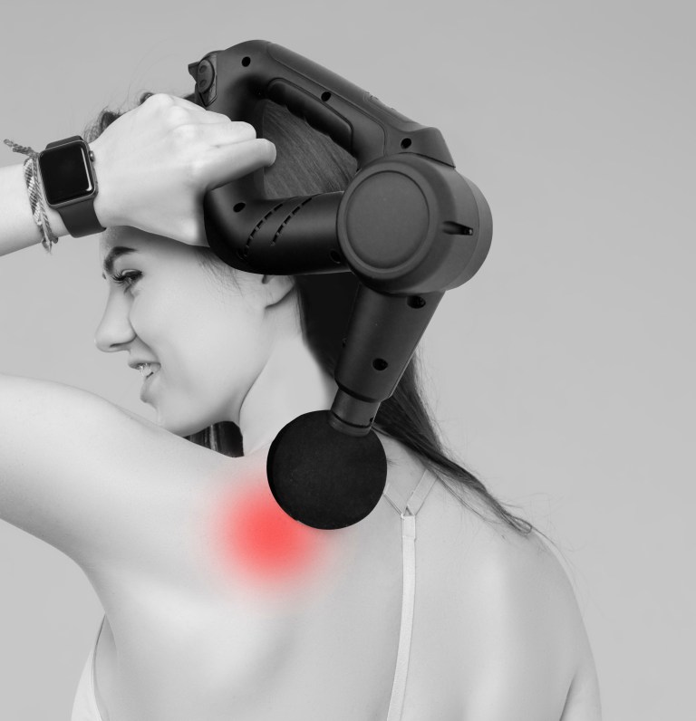 Woman using massage gun on sore shoulder