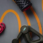 Massage gun and foam roller on exercise mat