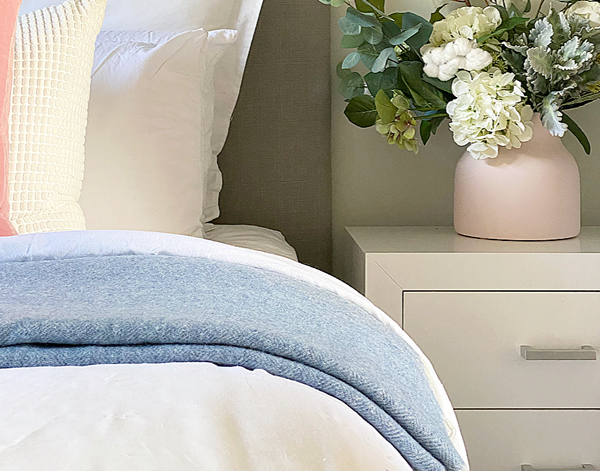 Neatly made bed with flowers on bedside table