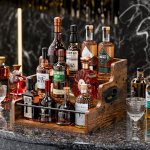 carla home 3 tier liquor bottle display shelf rack bar organizer for whiskey, wine, coffee syrups, spirits & bottles Wooden caddy filled with assorted whisky bottles