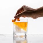 Hand garnishing whisky cocktail with orange peel