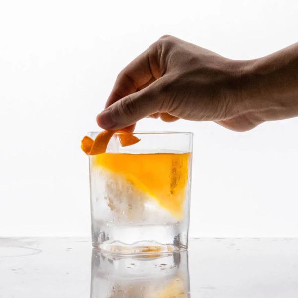 Hand garnishing whisky cocktail with orange peel