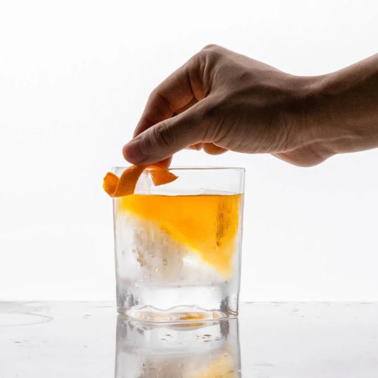 Hand garnishing whisky cocktail with orange peel
