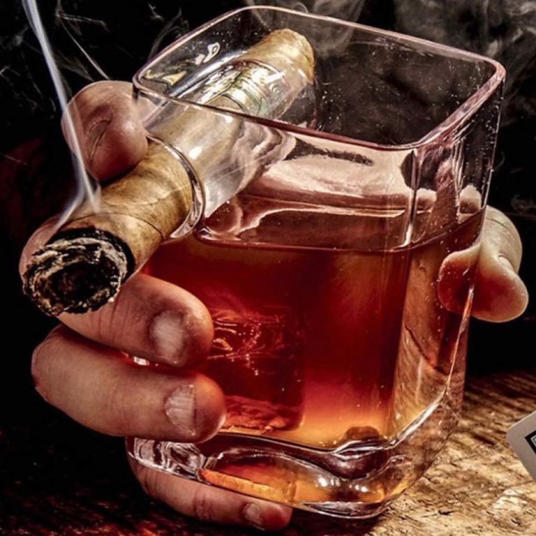 Hand holding whisky glass with lit cigar