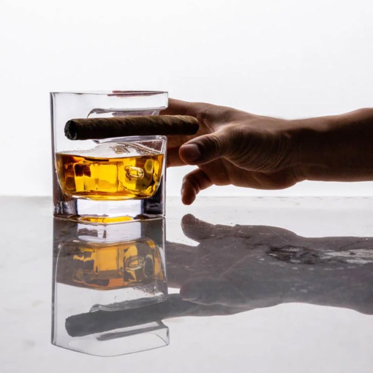 Hand holding whisky glass with cigar on rim