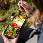 Person eating fresh salad from metal lunchbox outdoors