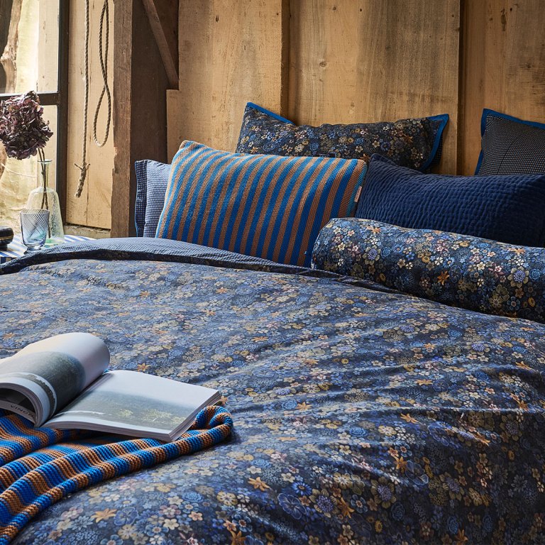 Floral blue bedding with striped cushions in rustic bedroom