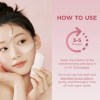 Woman applying clay mask holding skincare bottle