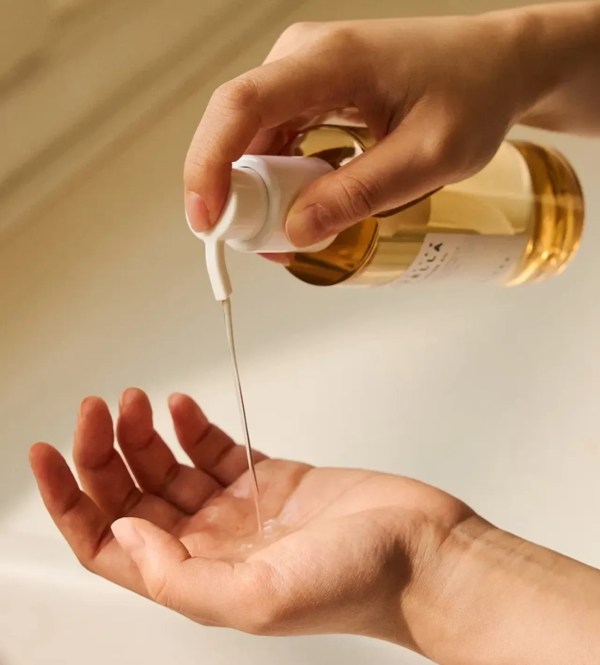 Hand pouring body oil from pump bottle