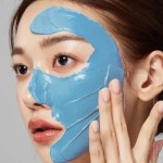 Woman applying blue facial mask skincare treatment